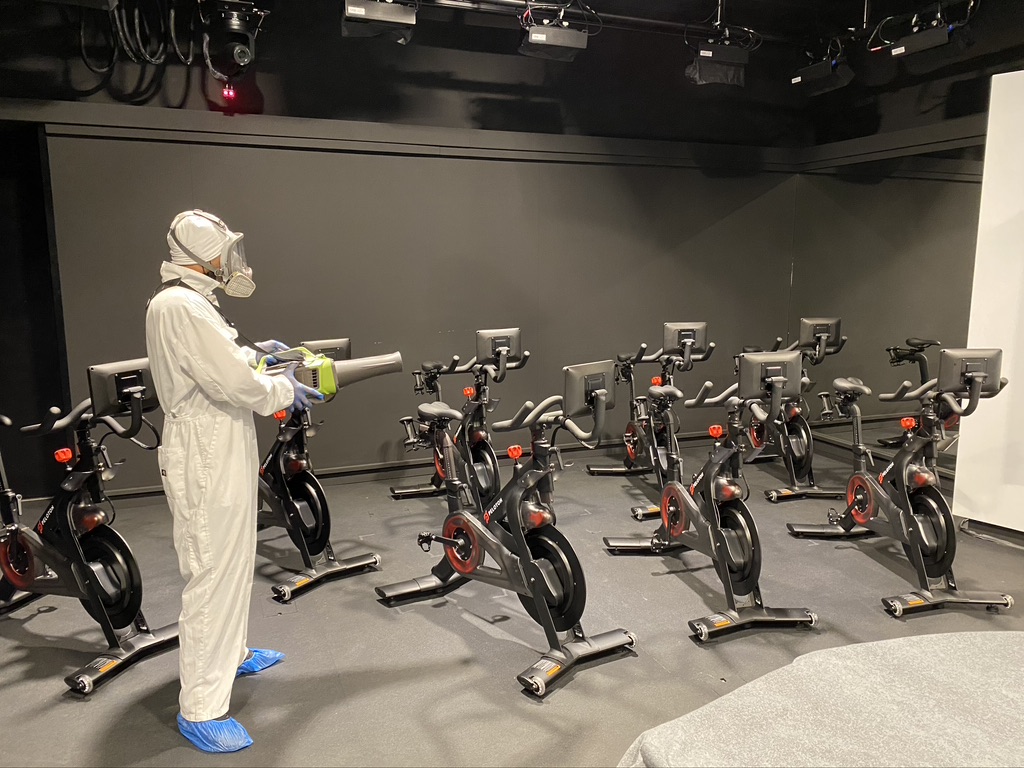 Technician performing electrostatic disinfection in London fitness studio, sanitising gym bikes with hospital-grade misting equipment commercial cleaning services London Akacleaning ltd